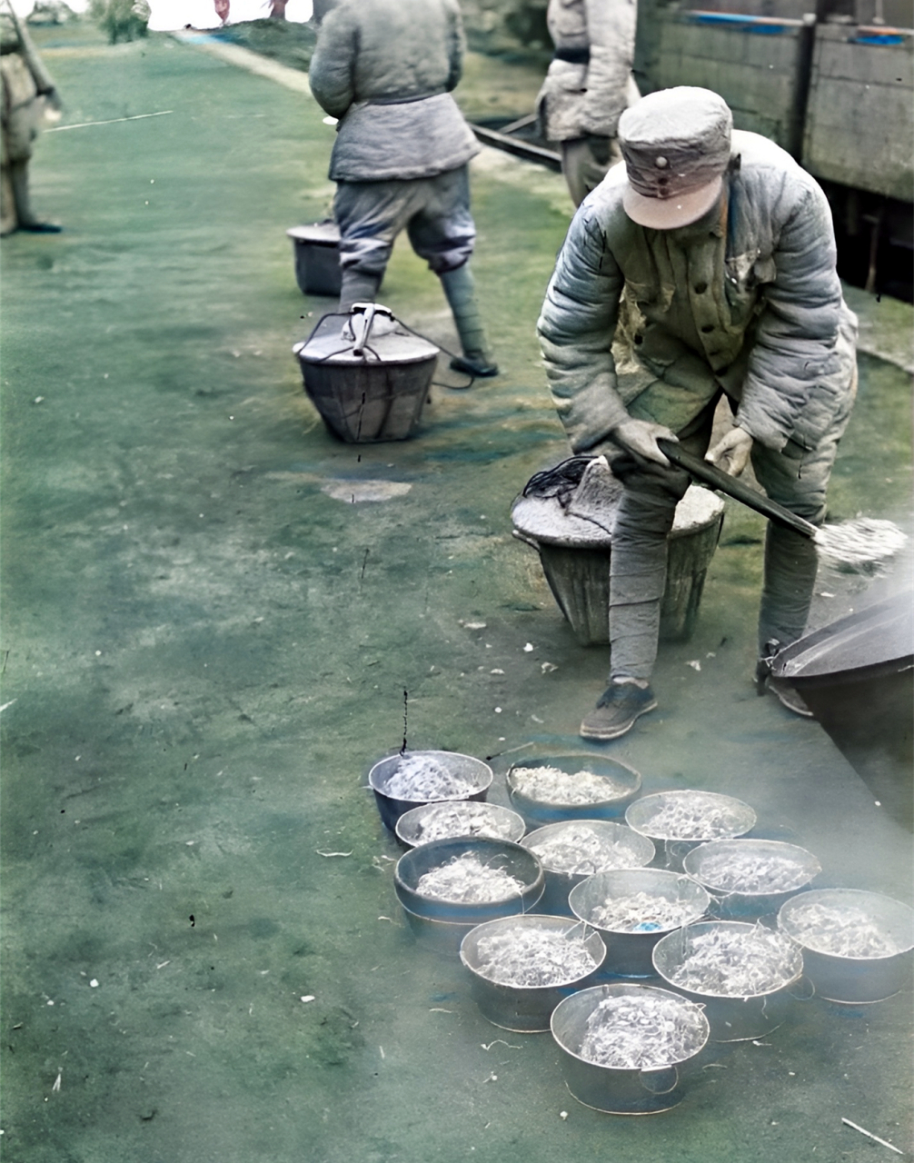 一名炊事班的士兵正用大勺从一口大锅里向外舀菜