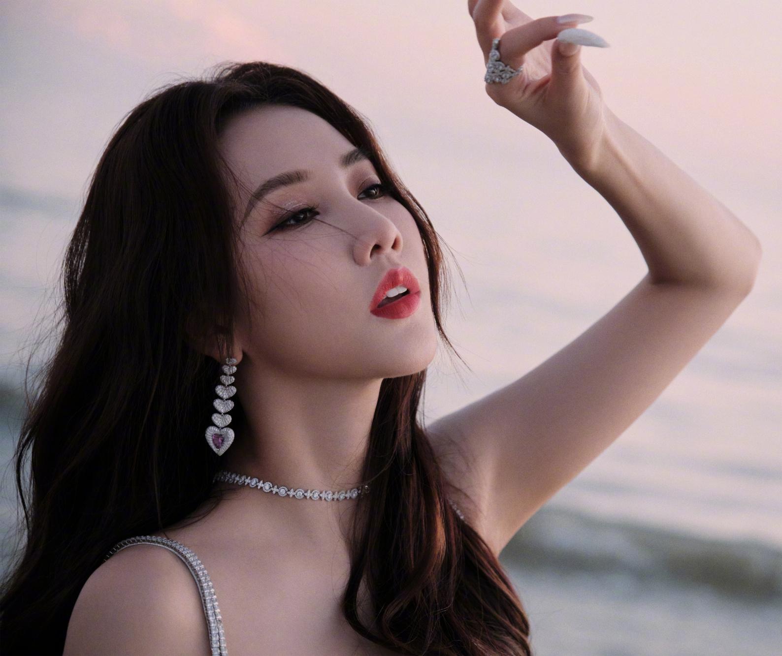 就像图中弦子身着白色长裙,耳戴精致耳环,在海边的阳光下悠然自得,静