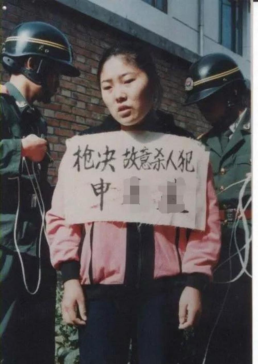 照片中,女死刑犯申某某站在寨墙之前. 她穿着粉色运动服和黑色长裤.