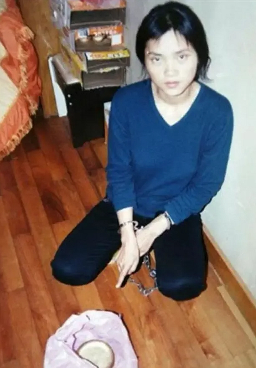 在一张十一年前的老照片中,一名戴着手铐的女子指着地上塑料袋里的