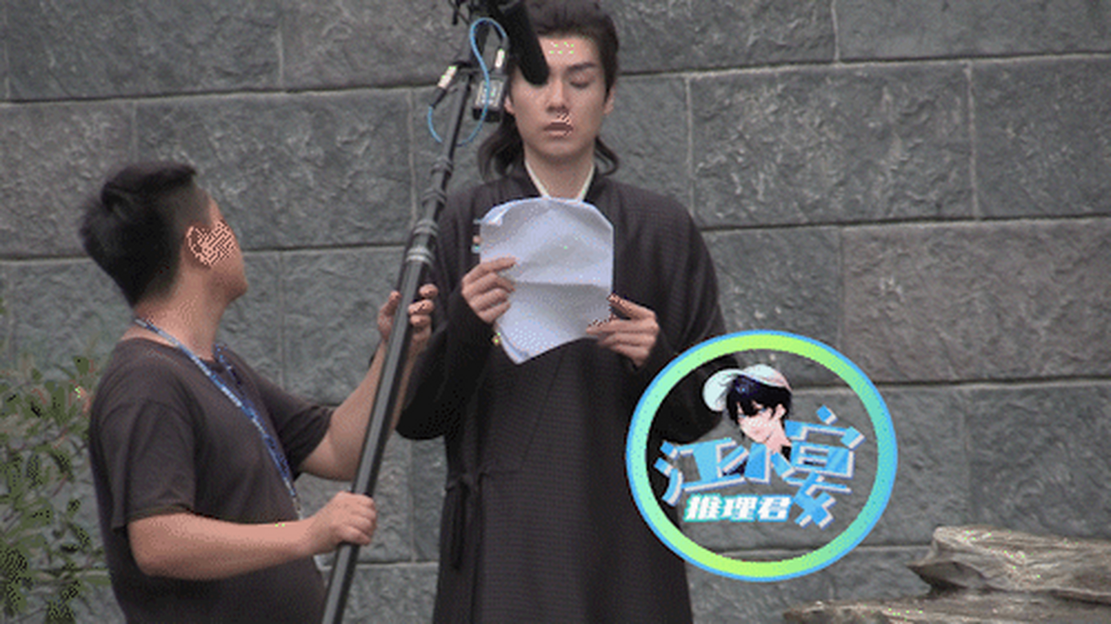 他身穿深棕色古装长衫,正站在一处户外空地上录音,胡一天盯着手里的