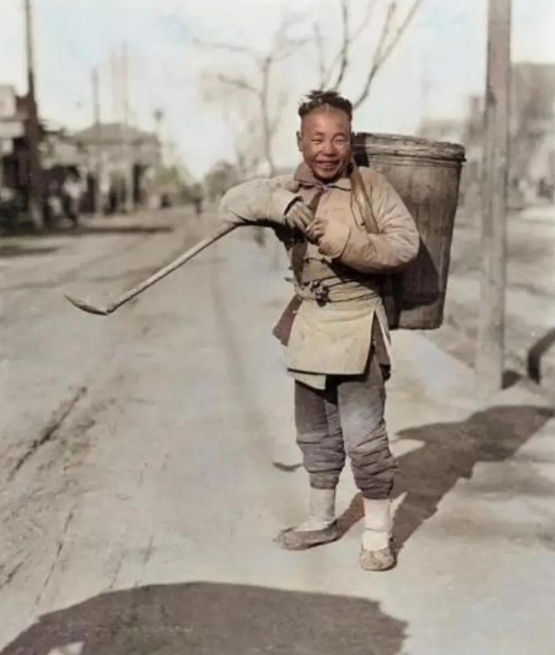 照片拍摄于民国时期,照片中的男孩脚踩着泥土,背着一个沉重的粪筐