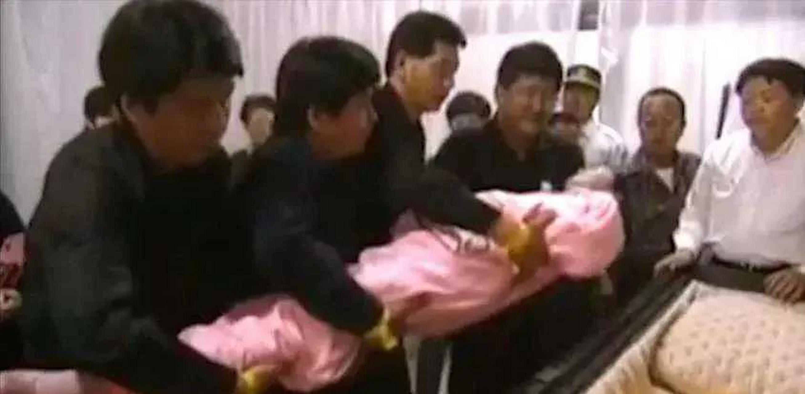 1995年泰国清迈,邓丽君遗体正被入殓师放入棺椁,她身穿粉红寿衣身体
