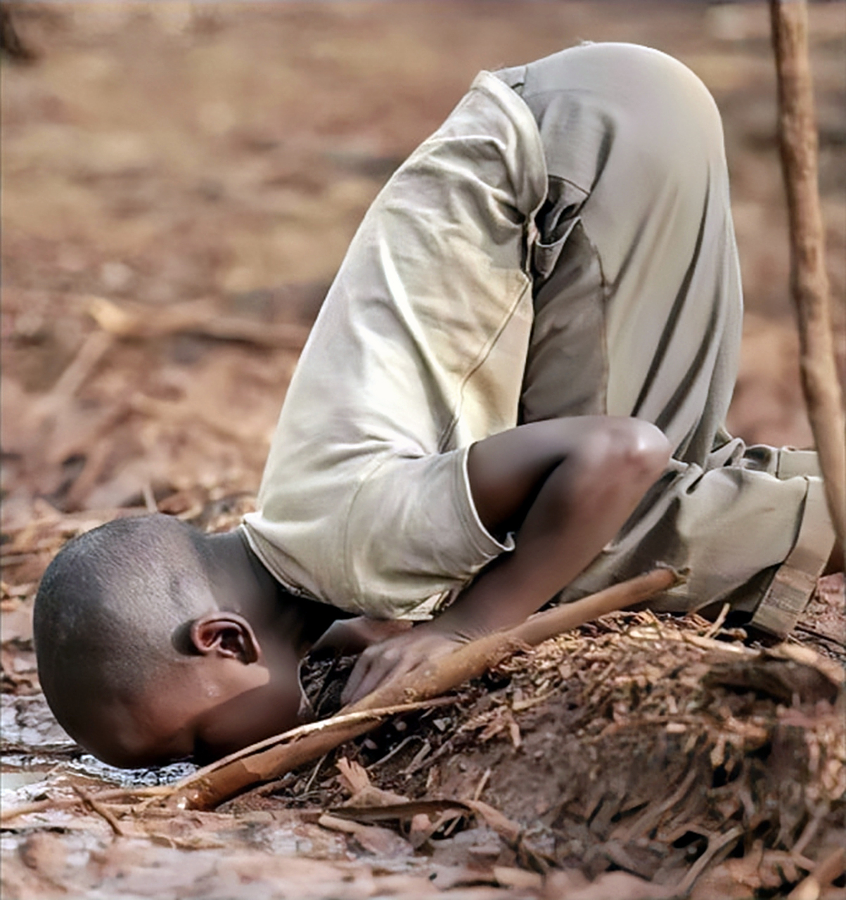 一名饥渴难耐的非洲小男孩正俯下身子舔舐河沟里残存的脏水