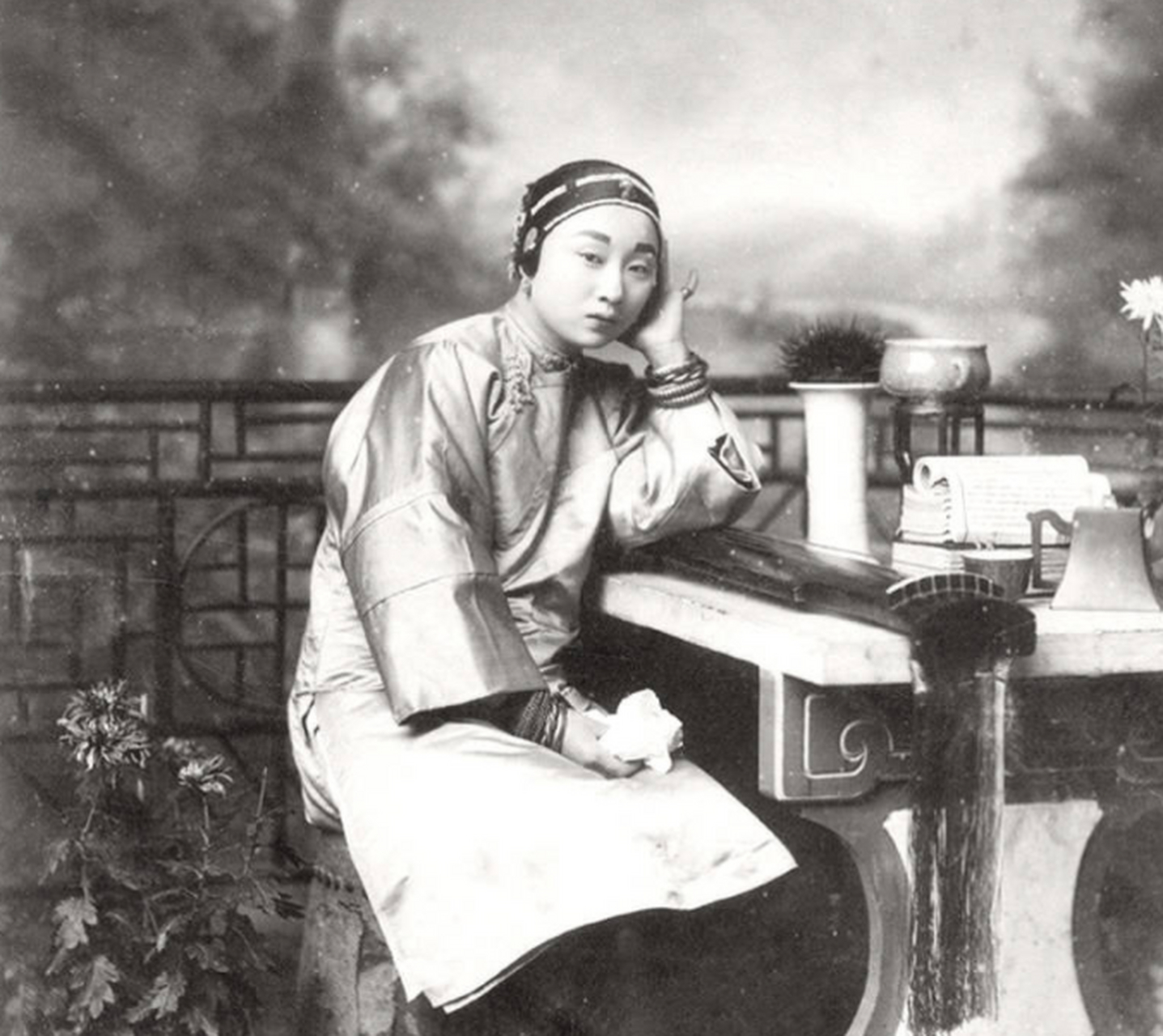 清朝老照片:照片中的女子衣着华丽,配饰讲究,面容姣好,左手托腮,面部