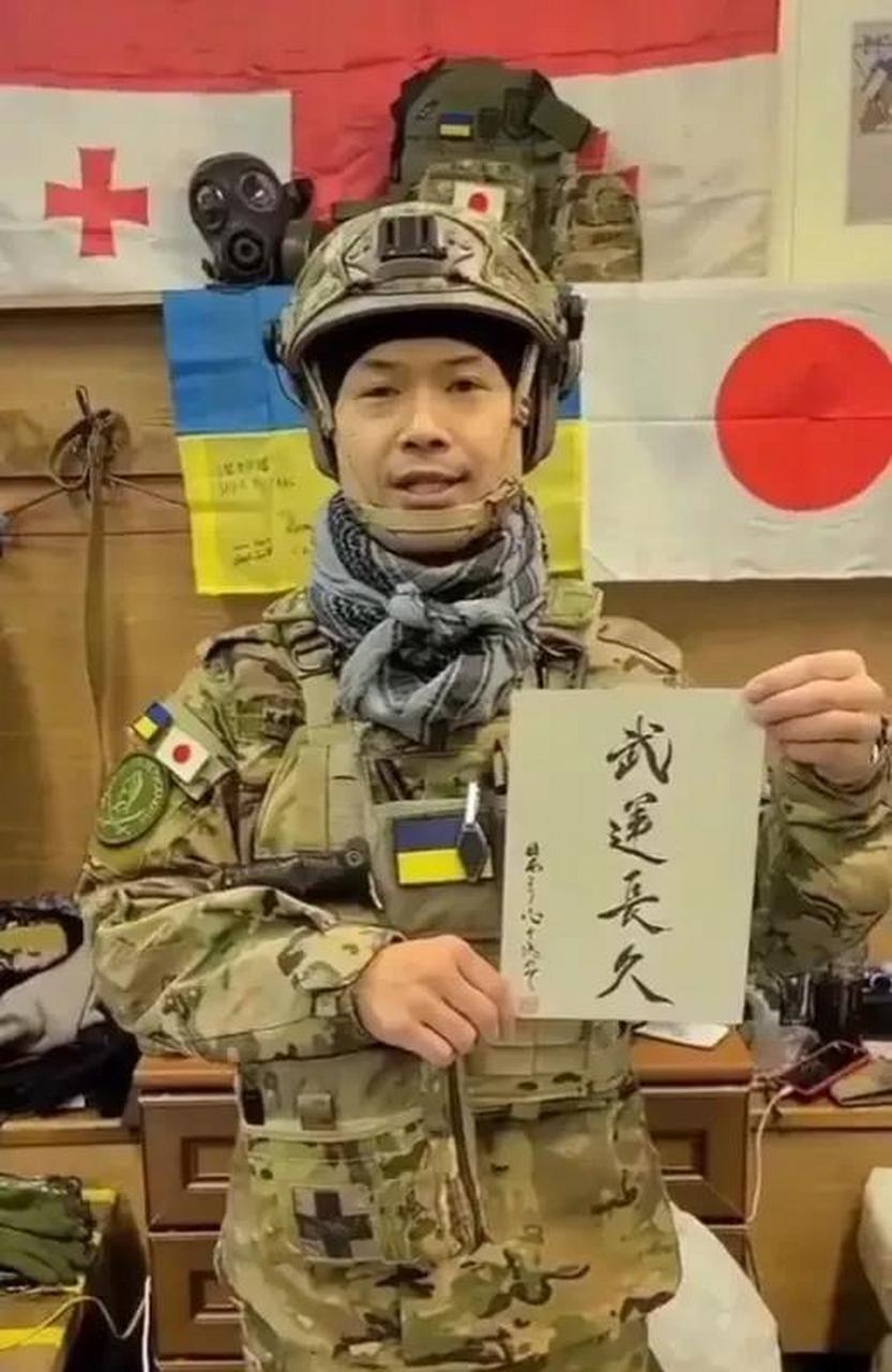 这名日本雇佣军举着"武运长久"的牌子,后面挂着日本"膏药旗"和乌克兰