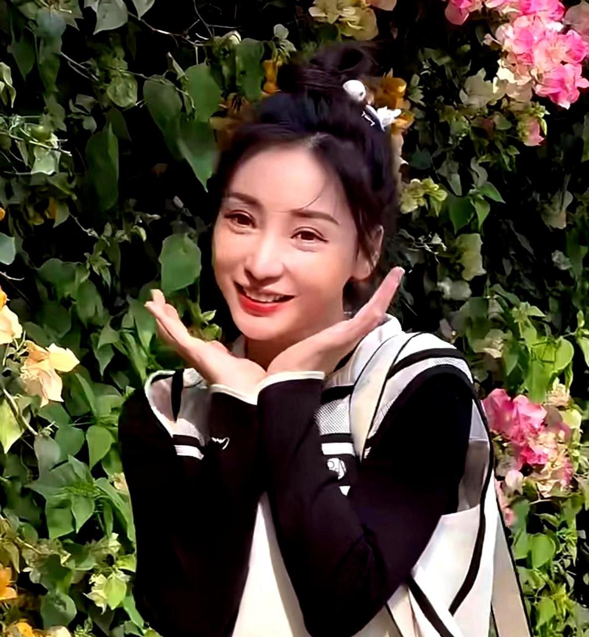 柳岩在花墙旁摆姿势拍照,双手托脸卖萌,笑容自然灿烂,散发着出游的