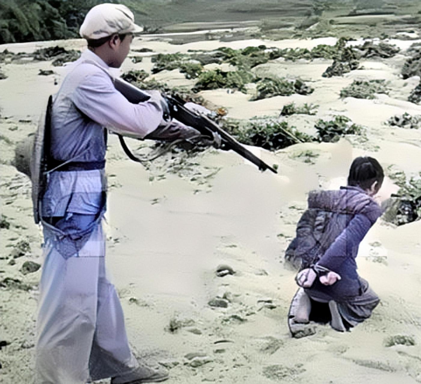 1952年,解放初期,一名头戴斗笠的解放军战士用枪指着一名被绑起来背