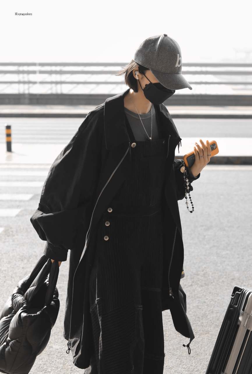 黑色风衣外套搭配条纹工装裤,头戴灰色棒球帽,黑灰色造型的小配饰点缀