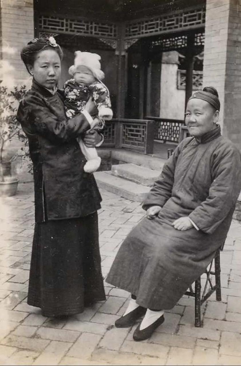 清朝末期的一对婆媳的照片,婆婆坐在椅子上,而儿媳妇则抱着孩子,婆婆