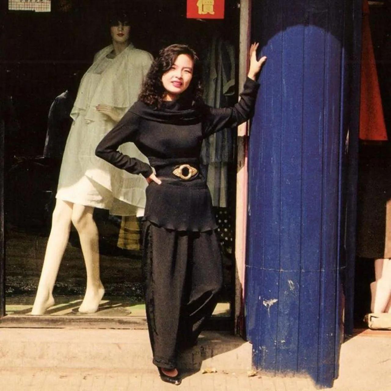 年代,一家出售时装服饰的店铺前,一位时尚打扮,颜值惊人的女老板站在