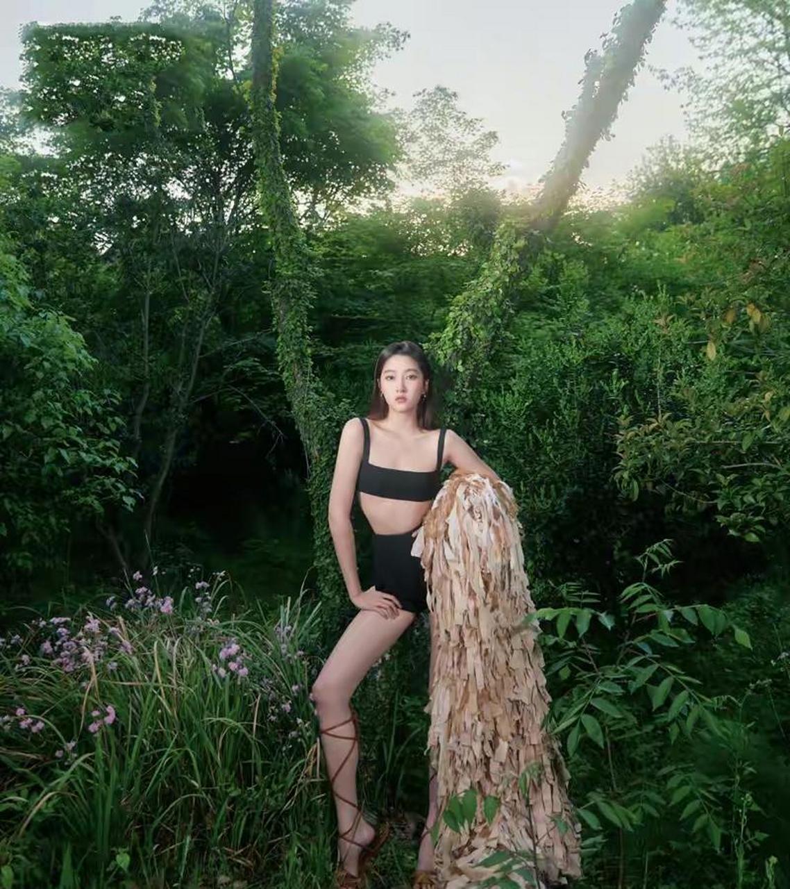 背景是一片碧绿的树木草地,关晓彤身着黑色分体泳衣秀身材,大长腿过于