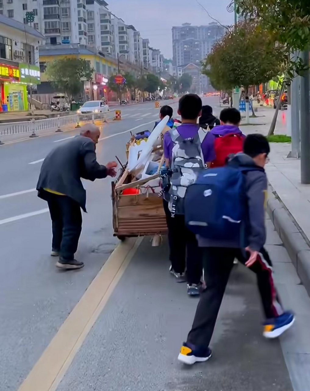 老人拉着收废品车子艰难上坡,几名小学生热心帮老人拉车,老爷爷为了