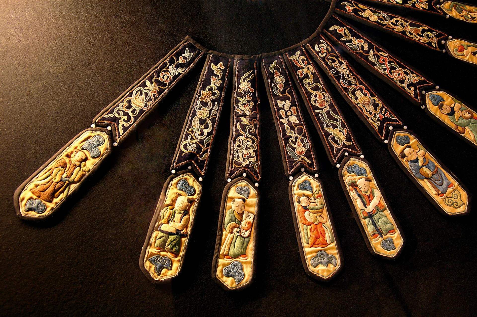 图为19世纪的双色缎打籽平金绣人物柳叶式云肩,内层在黑缎地上以平