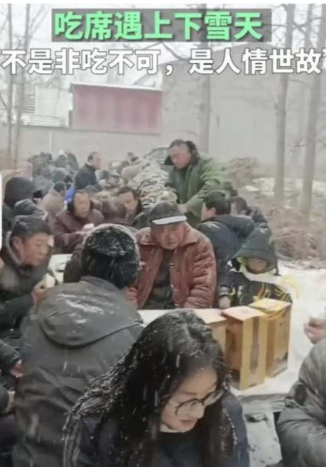 视频中,亲友们围坐在雪地里吃席,个个冻得瑟瑟发抖,大伙就着飘雪吃着