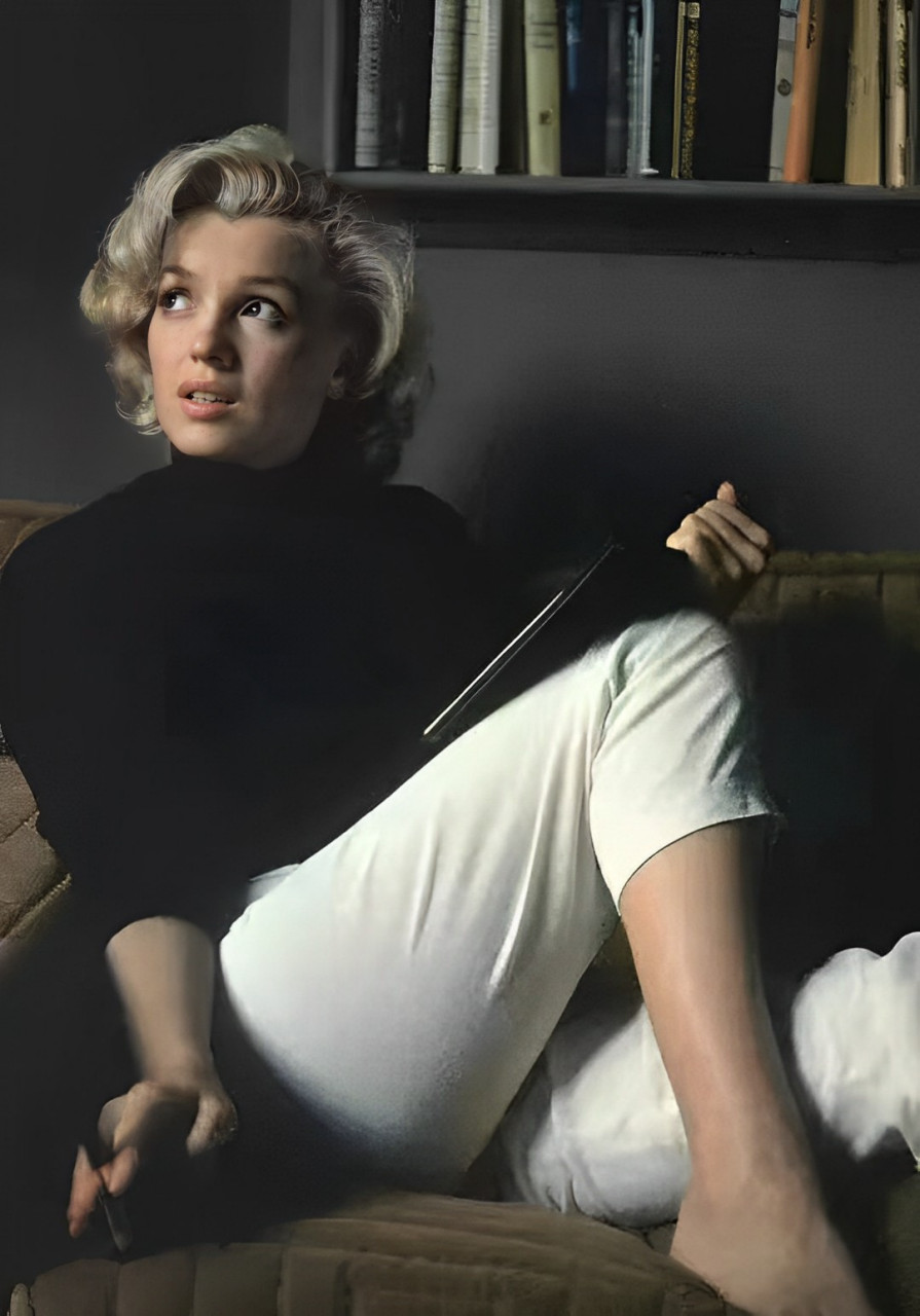 照片中梦露穿着黑色上衣,白色长裤,拿着一本本子似乎在书写着什么