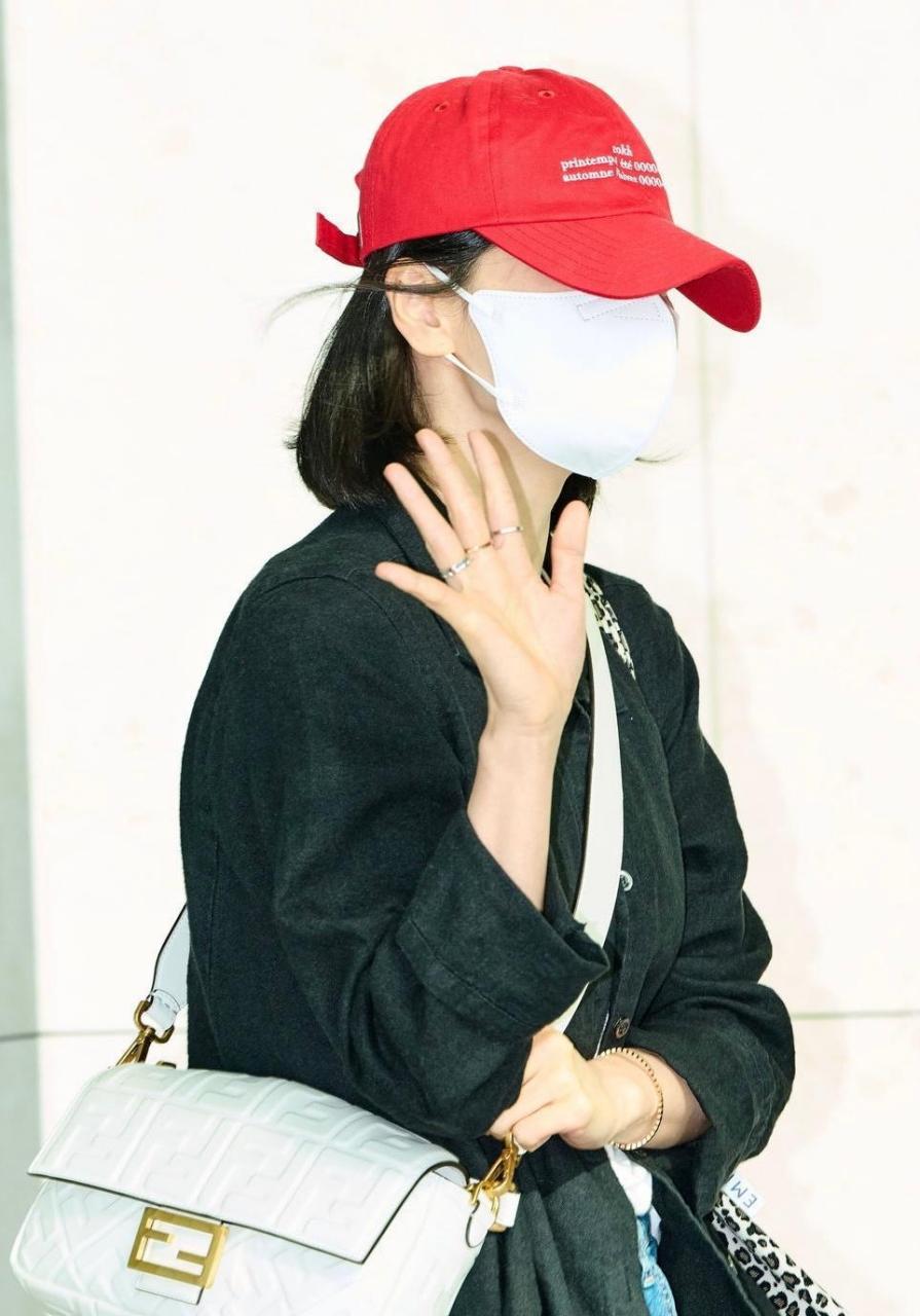 宋慧乔机场街拍,她身穿纯黑长外套配以红色棒球帽,下搭丹宁裤与小白鞋