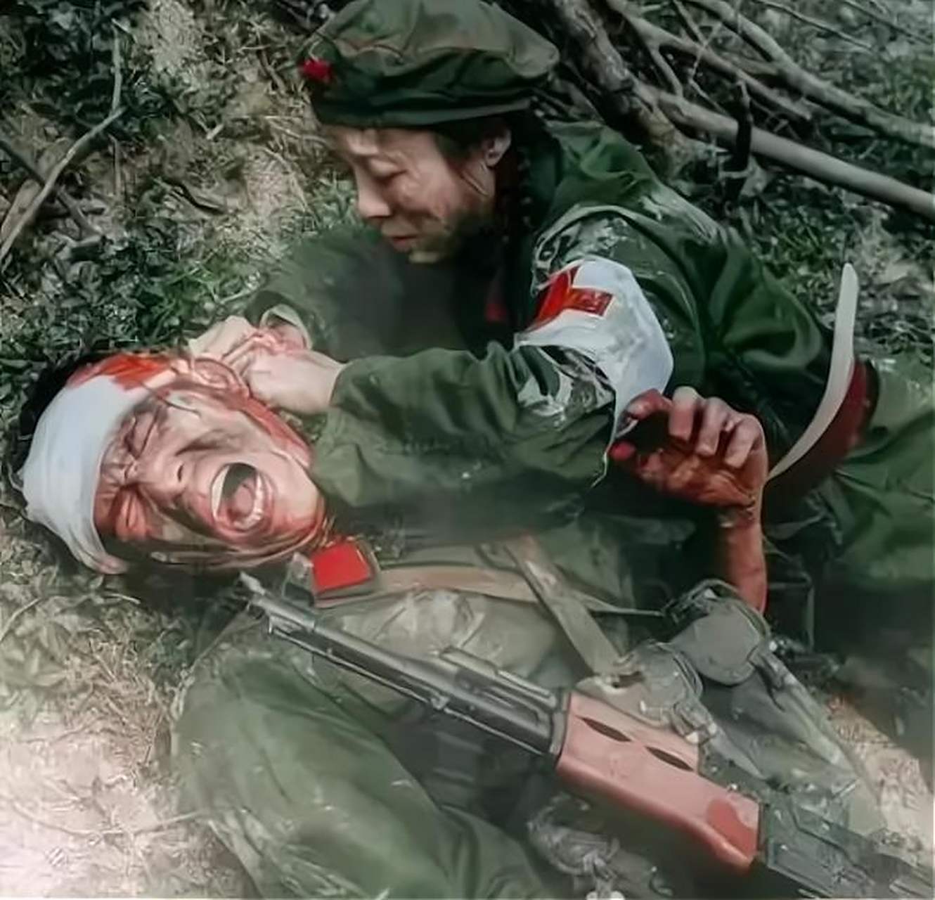 1979年老山战役中,一名年轻的战士躺在地上,一位护士正在给他包扎头部