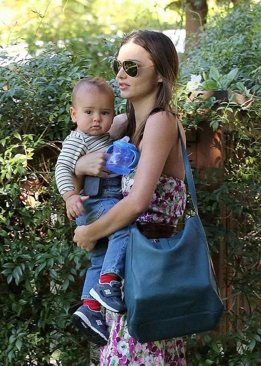 2012年,超模米兰达·可儿身穿抹胸碎花裙抱着儿子小开花出街.