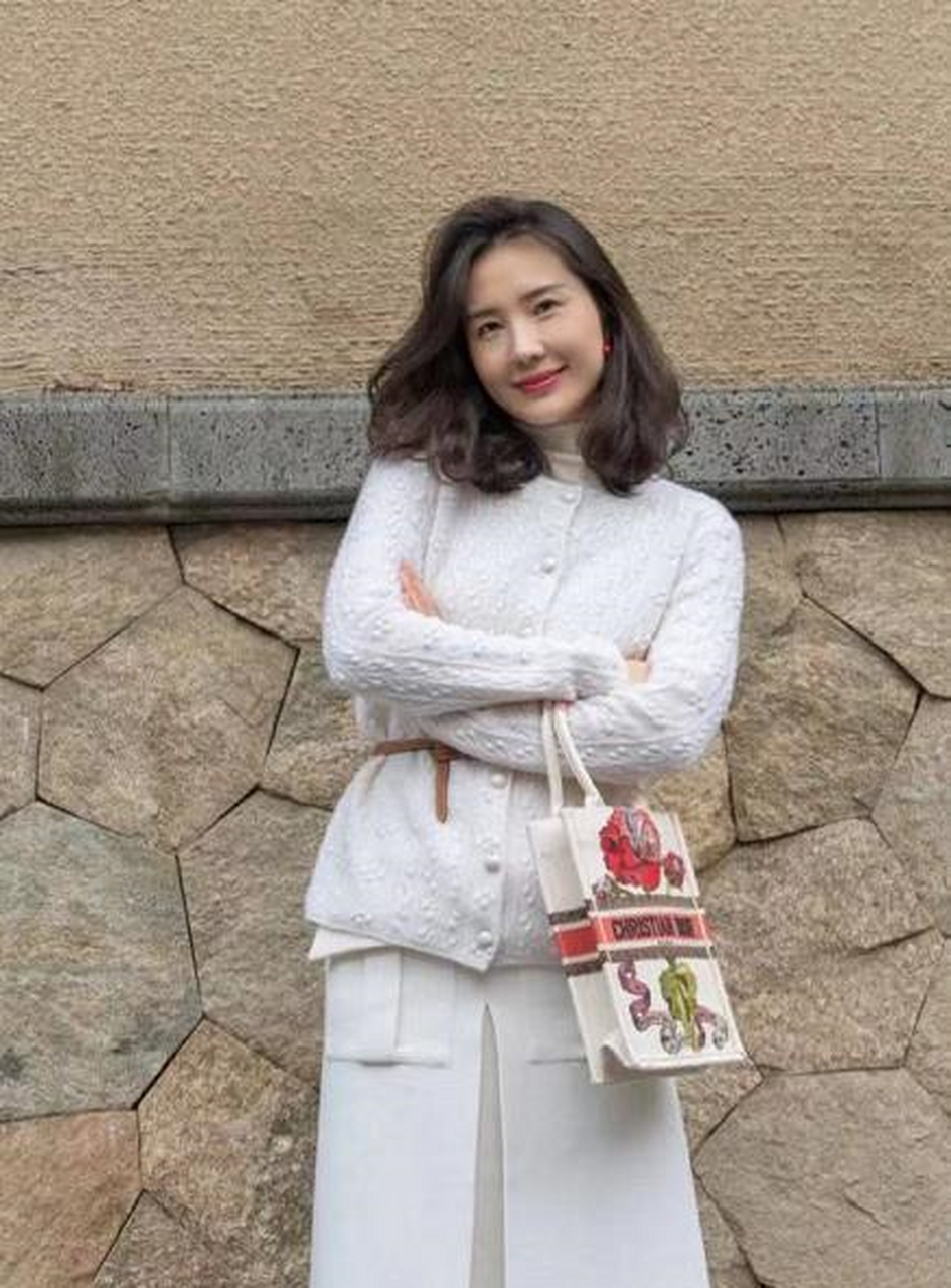 野外露营的董花花高扎丸子头,身穿浅色羽绒服黑色长裤,坐在篝火前的她