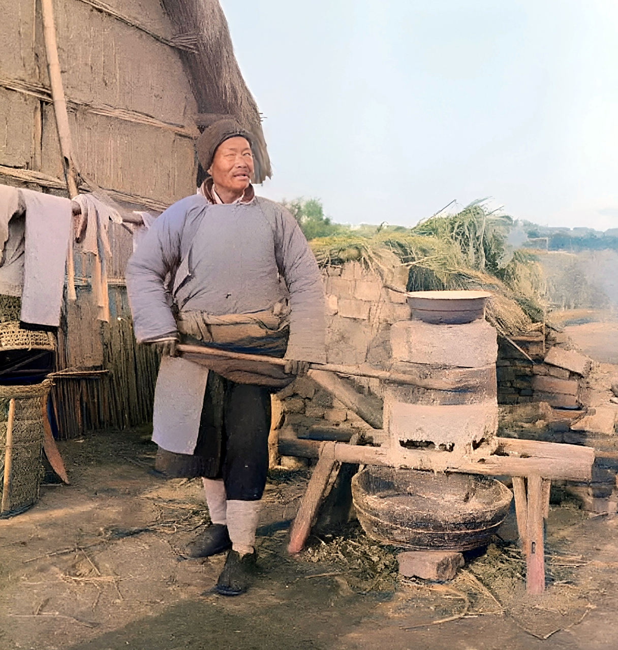 老人一边推磨,一边将盆里用水泡的粮食舀到磨眼里.