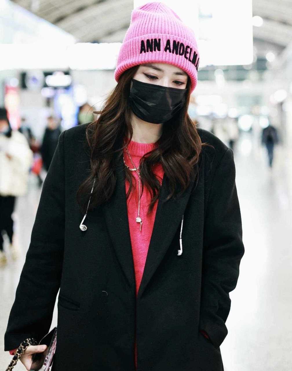 徐璐机场私服穿搭,身穿黑色大衣内搭粉红毛衣,头戴粉色毛线帽,皮裤