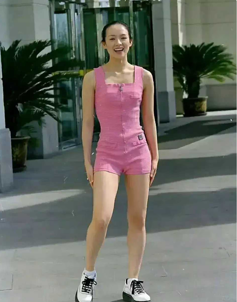 照片中的章子怡身穿一件粉色连体衣,脚上穿着白色运动鞋.