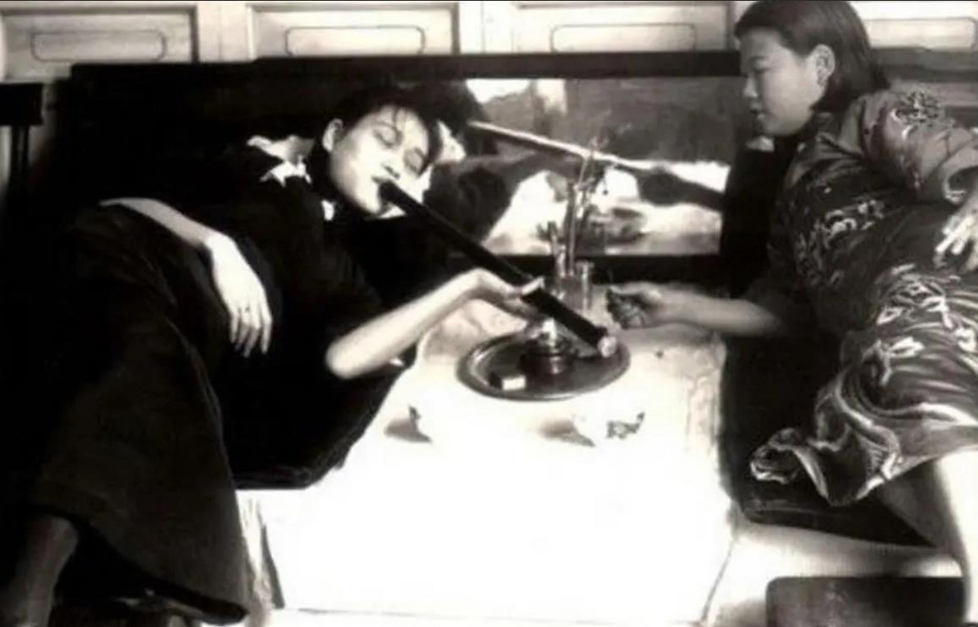 历史老照片,两个女子躺在床上吸食鸦片,看起来非常慵懒,她们的身体