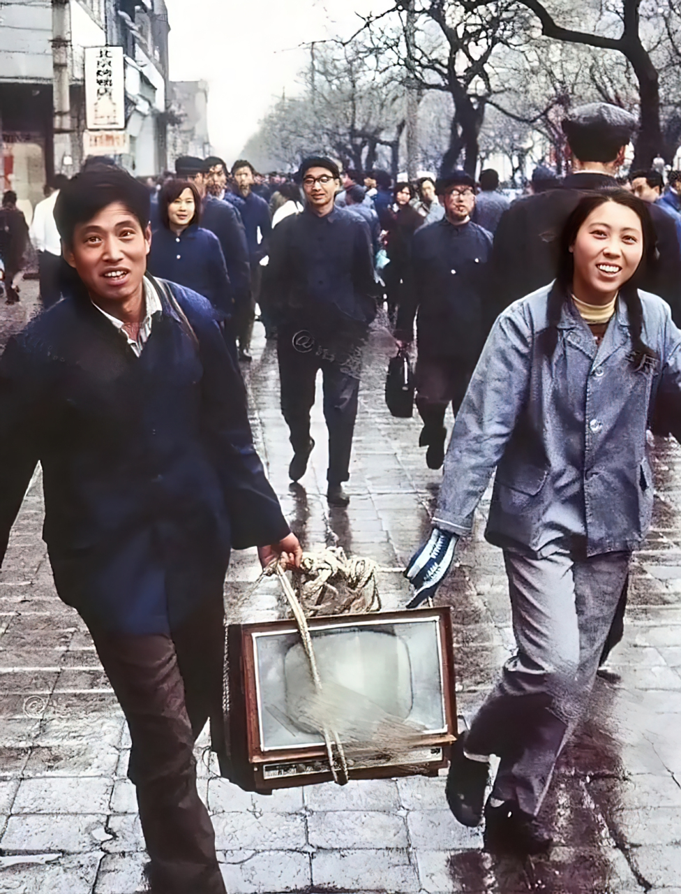 70年代,北京街头,一对年轻夫妇正高兴地抬着他们新买的黑白电视回家.