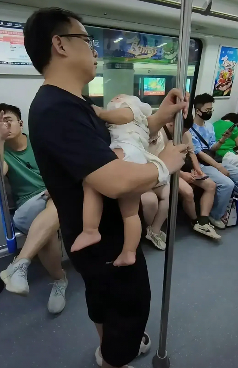 一位中年男人,抱着一个幼小的孩子乘坐地铁,没有了座位.