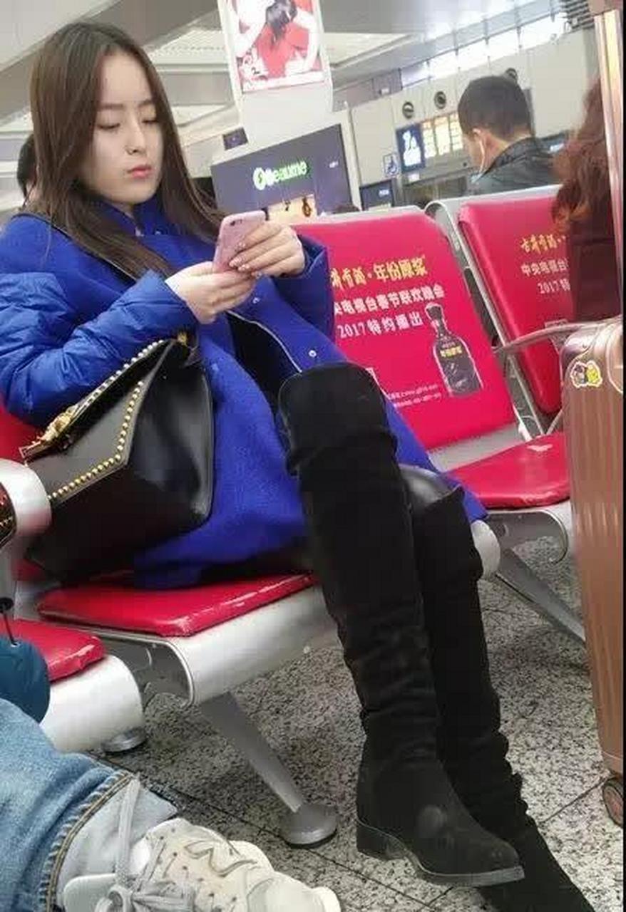街拍:紧身黑皮裤搭黑长筒靴的漂亮姑娘,车站等车看手机打发时间