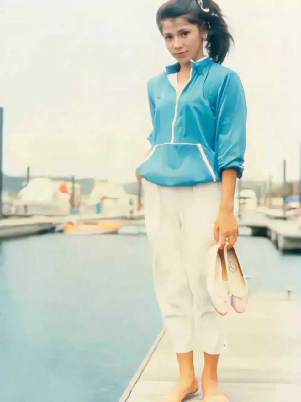 80年代,翁美玲站在海边,赤着脚俏生生地站着,一双鞋子被她提在手中