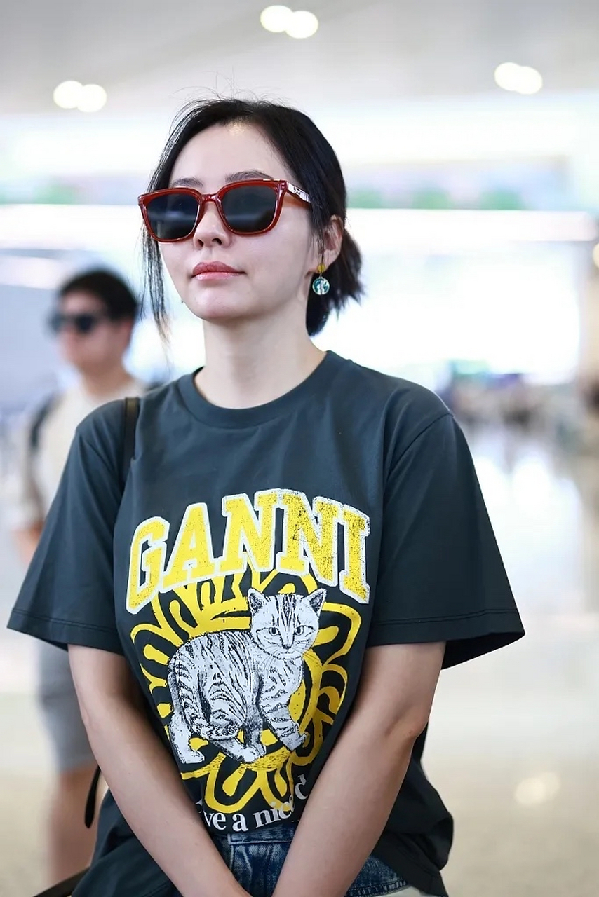 张靓颖最新机场照来了,她穿了一件黑色的短袖t恤,这t恤胸前的黄色图案