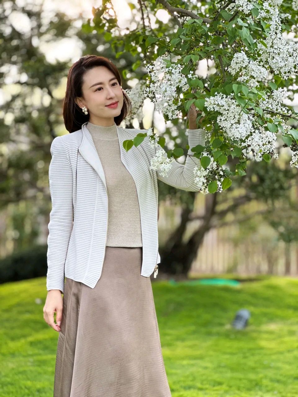 主持人张蕾丁香树下摆拍造型太美了,穿米色开衫内搭中高领针织衫打底