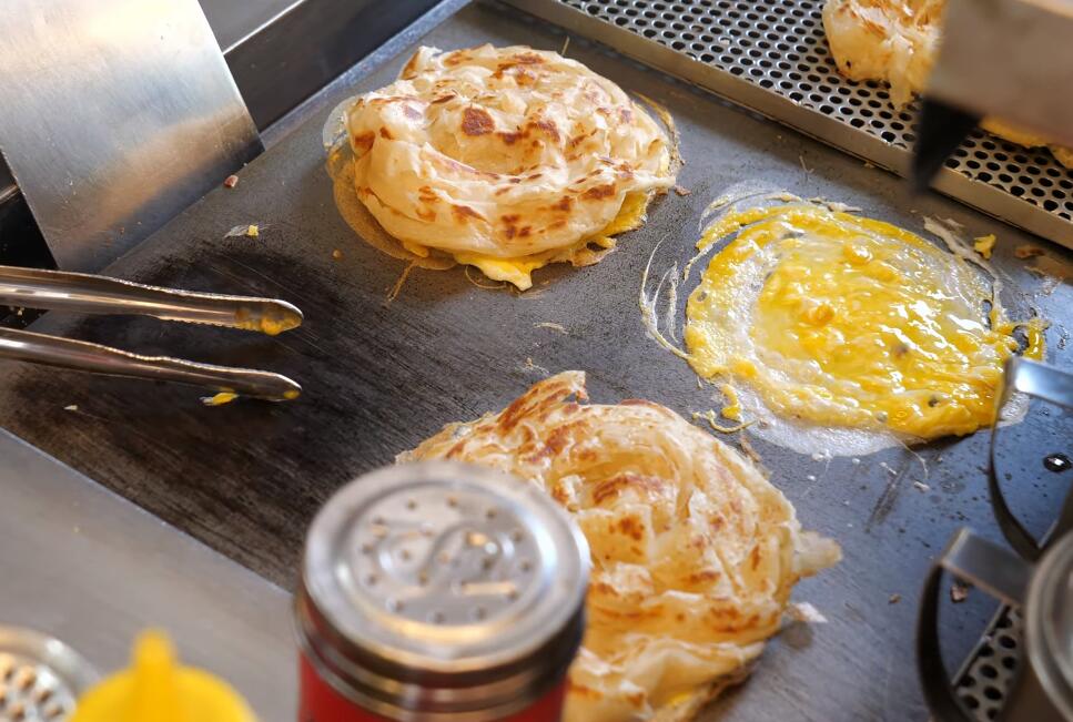 街头小吃铁板鸡蛋饼,两块饼夹着煎蛋和玉米粒,挤上番茄酱食用