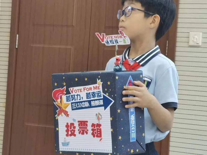 自制的投票箱上,系着红领巾的候选人卡通形象举着星星火炬,还镶嵌着