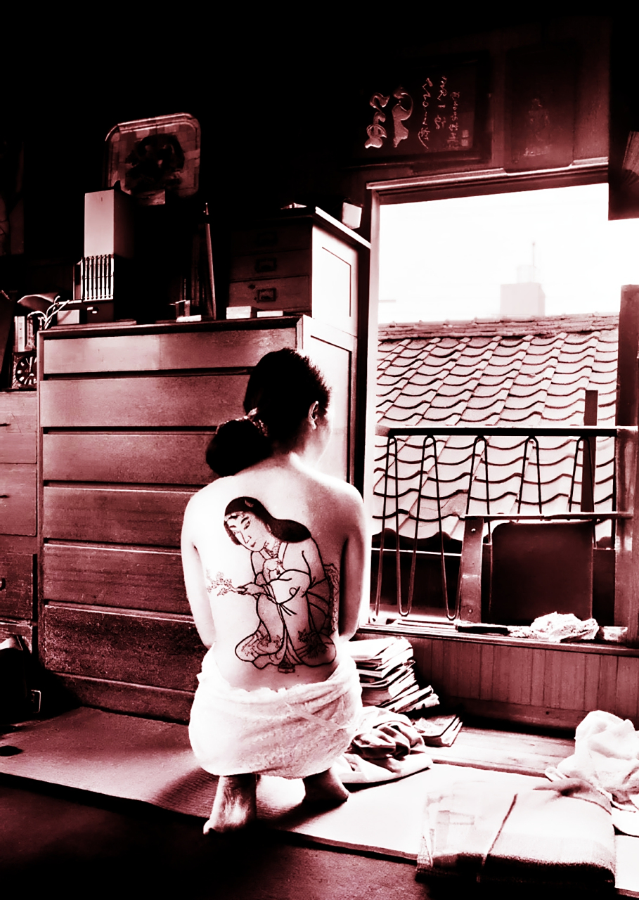 照片中,妹子披着浴巾,光着后背!纹身艺术家正坐在上面并在上面工作!