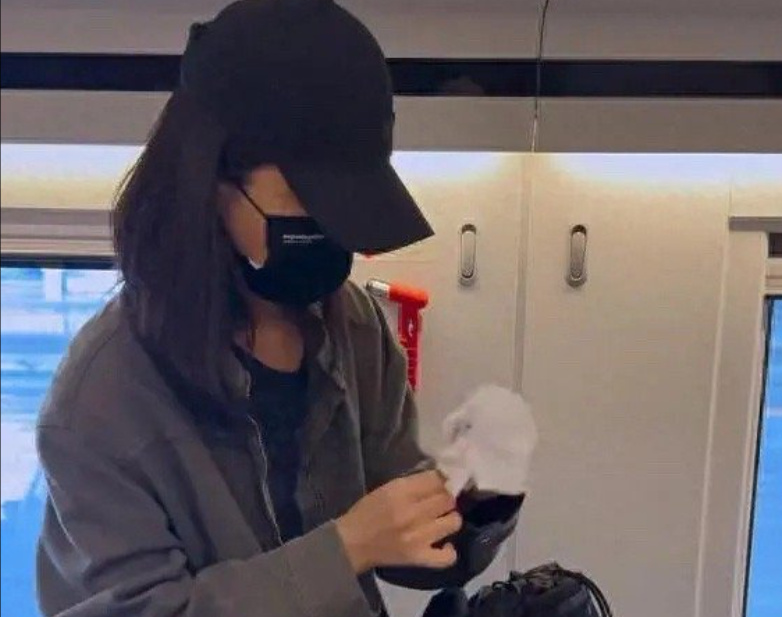 乘客在火车上使用手机，戴口罩和帽子。