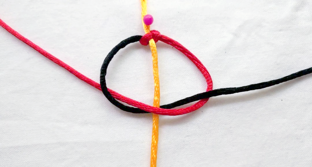 将黑色绕线穿过轴线下方的圈,并拉紧,即可完成半个平结的编织