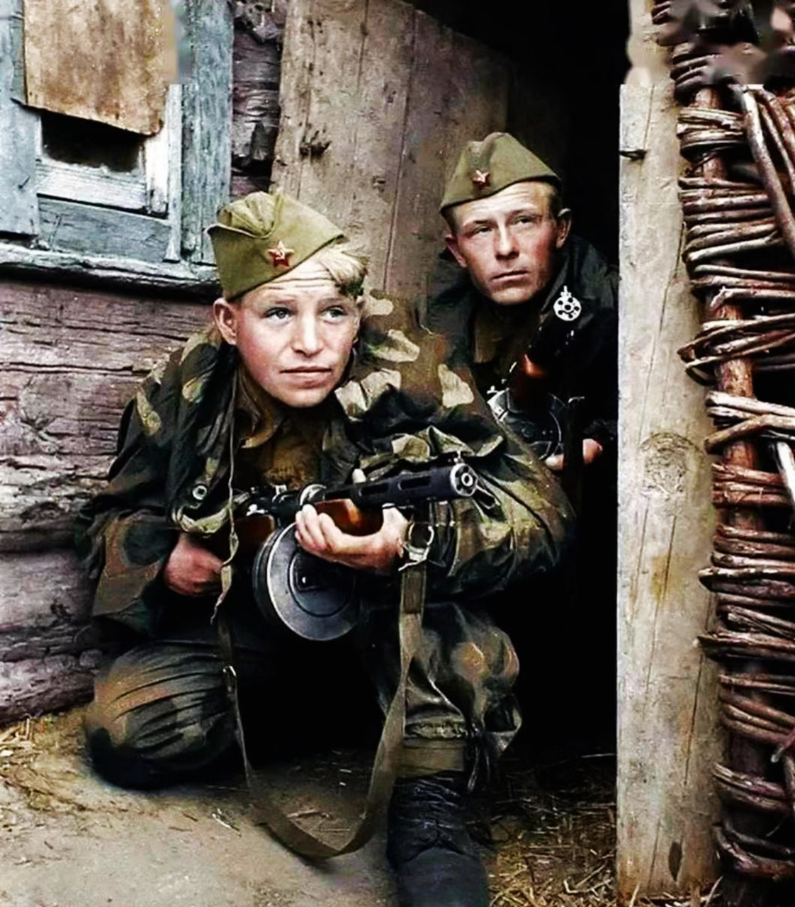 二战期间,两名苏联侦察兵蹲在茅草屋门口观察对面德军的情况.