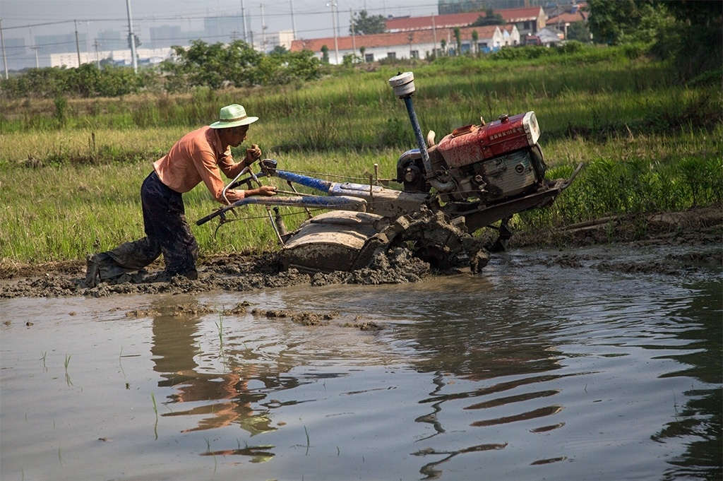 一位农民伯伯开着拖拉机,正在大田里进行打泥作业!