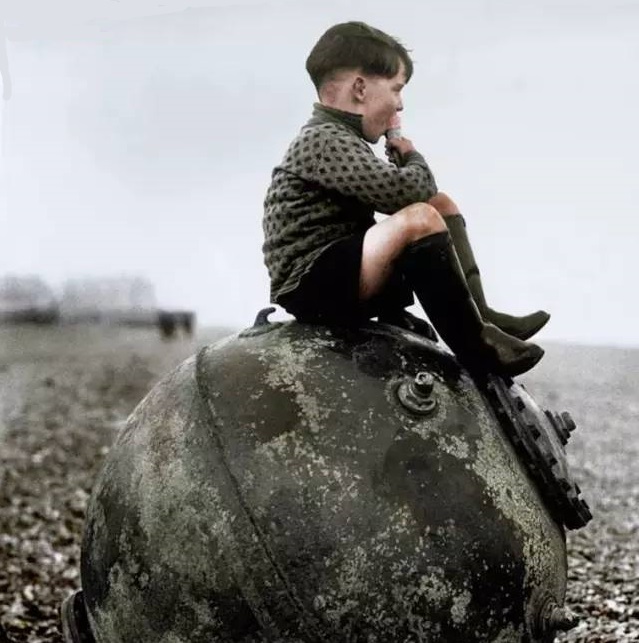 一名孩童坐在一颗水雷上面,天真无邪的他依然把武器当成了玩具.