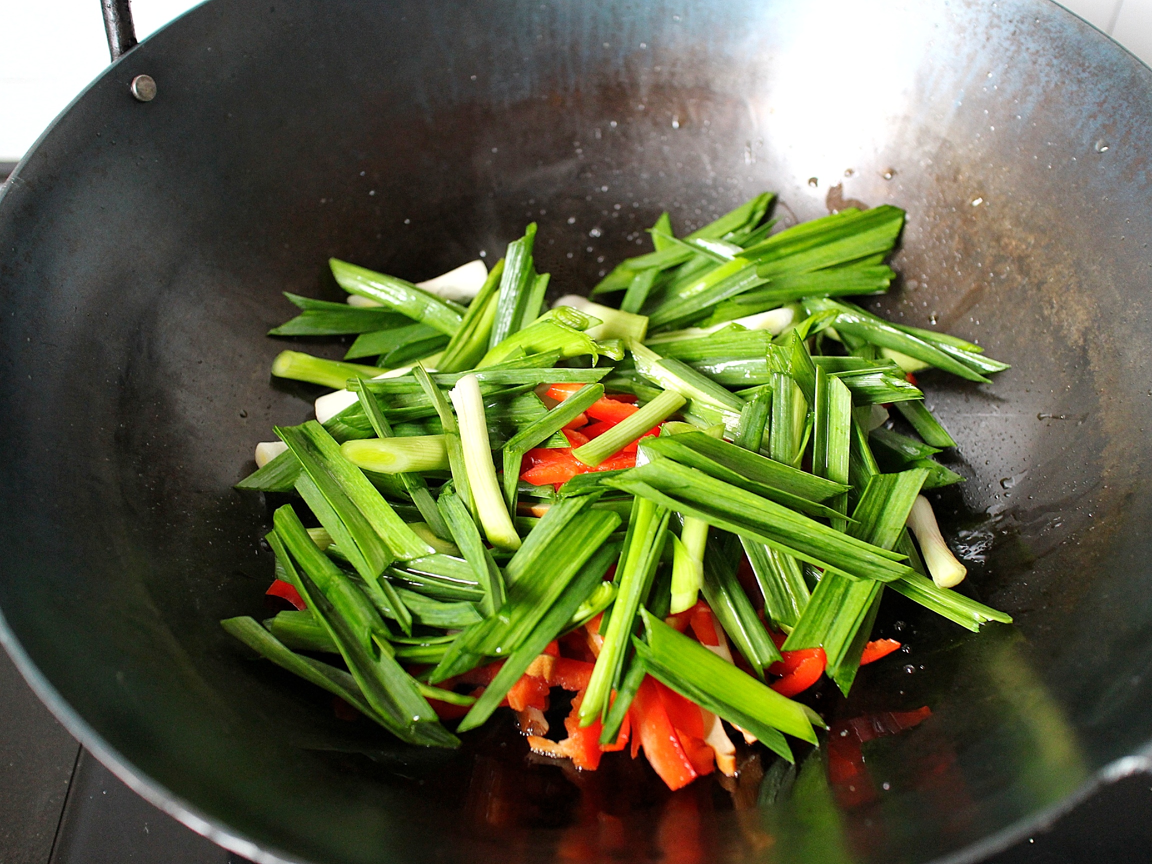 4,等蒜片炸到稍微泛黄后,我们把大蒜叶,红辣椒,香干一起倒入锅内,转