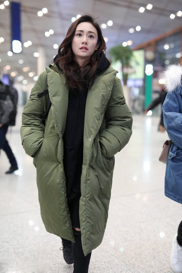 她身穿黑色连帽卫衣 绿色长款羽绒服,温暖简约.