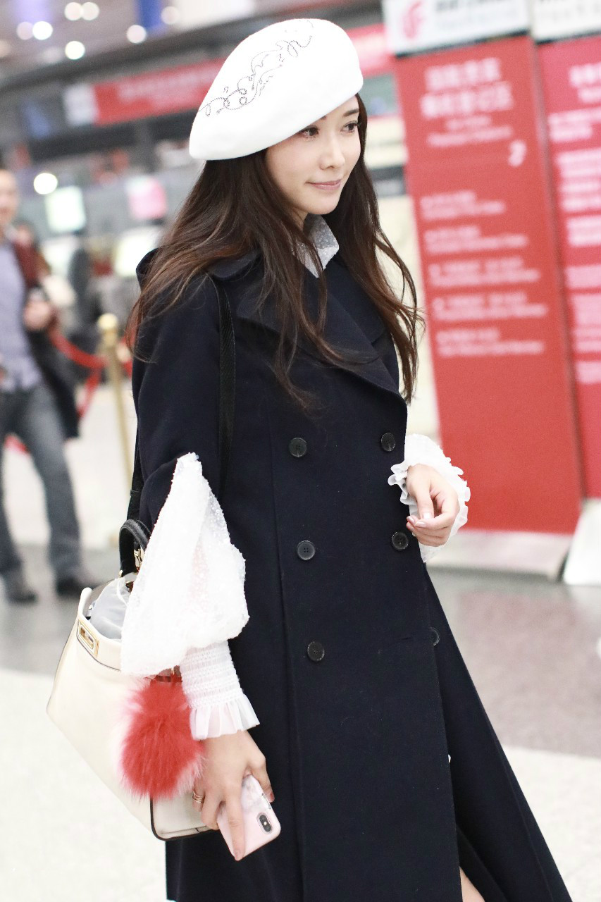 林志玲戴白色贝雷帽穿黑色长款大衣现身机场,皮肤白皙面带微笑