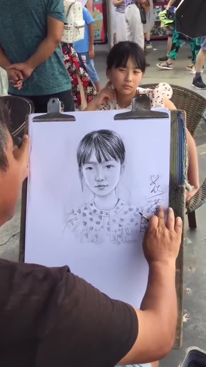 街头的画师正在给小女孩画肖像画,别说,整个神态画得还挺像的